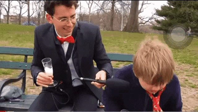 a man in a suit and bow tie is sitting on a bench with another man