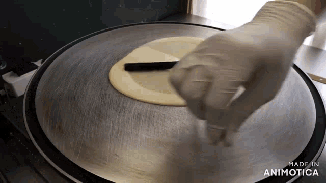a person wearing white gloves is making a tortilla on a stainless steel griddle