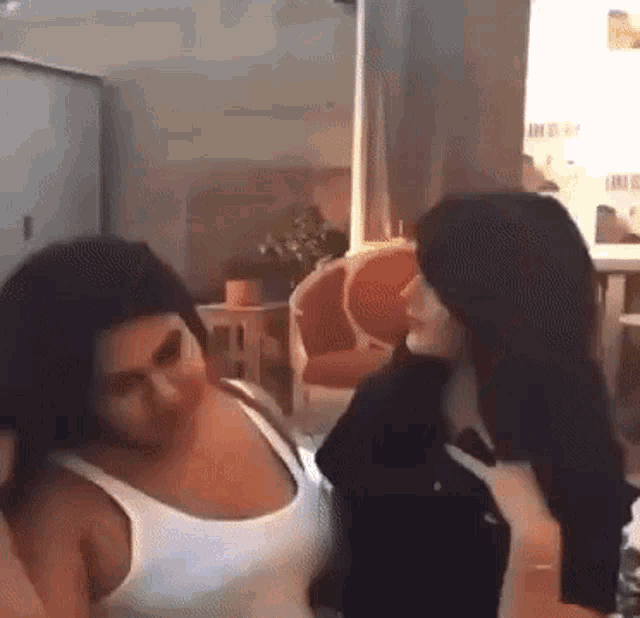 two women are standing next to each other in a room and talking to each other .