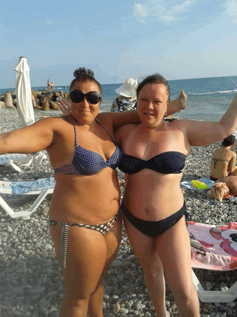 two women in bikinis are posing for a picture on the beach