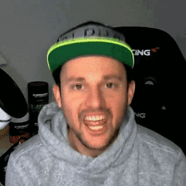 a man wearing a grey hoodie and a green hat with the word racing on it