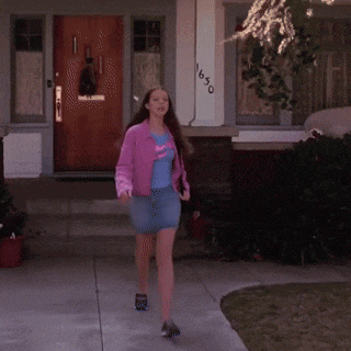 a woman in a pink jacket and blue skirt is walking in front of a house with the number 1650 on it