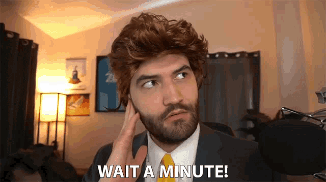 a man in a suit and tie says wait a minute in front of a microphone