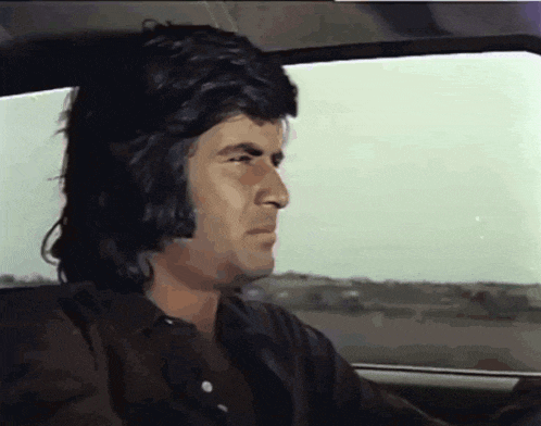 a man with long hair is sitting in a car looking out the window
