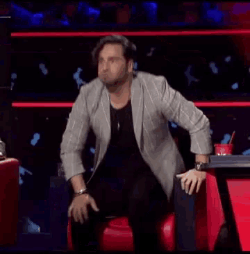 a man in a suit is sitting on a red chair in front of a blue background .