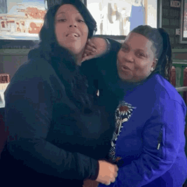 a woman in a blue jacket is hugging another woman in a black hoodie