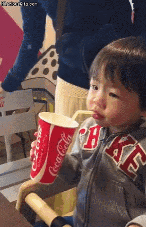 a young boy drinking from a coca cola cup