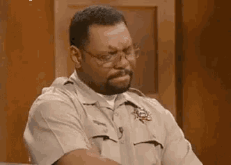 a man in a sheriff 's uniform and glasses is sitting at a table in a courtroom .