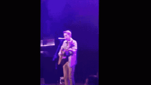 a man is playing a guitar on a stage with purple lights .
