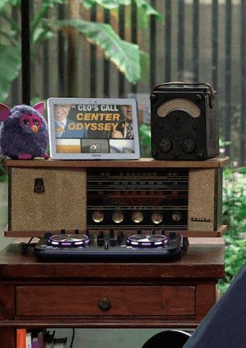 a purple furby sits on a table next to a radio