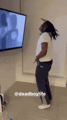 a man with dreadlocks is dancing in front of a television .
