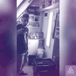 a man in a black shirt is standing in a room with a purple background and the word alive on the bottom