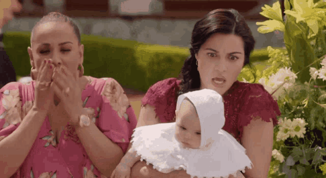 two women are holding a baby in a white outfit