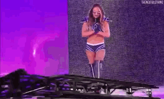 a woman in a wrestling outfit is standing on a stage in front of a purple wall .