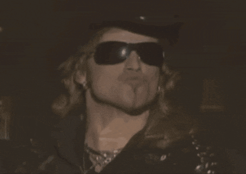 a man wearing sunglasses and a hat looks at the camera