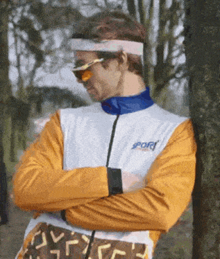 a man is leaning against a tree wearing sunglasses and a headband .