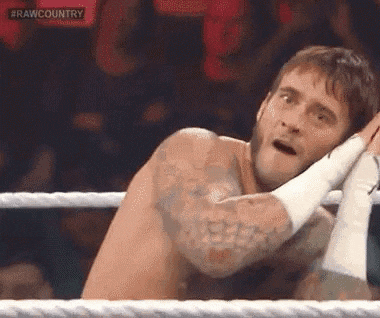 a shirtless wrestler is sitting in a wrestling ring with his hands on his head .