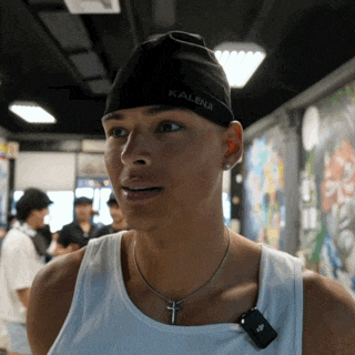 a man wearing a white tank top and a black kalenji hat