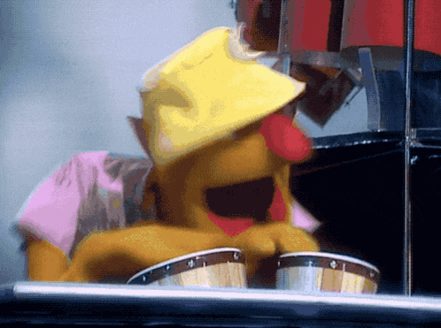 a muppet wearing a yellow hat is playing a drum set