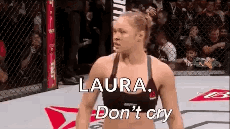 a woman is standing in a boxing ring with the words `` laura , don 't cry '' written above her .
