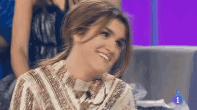 a woman is smiling while sitting on a couch with the number 1 in the corner .