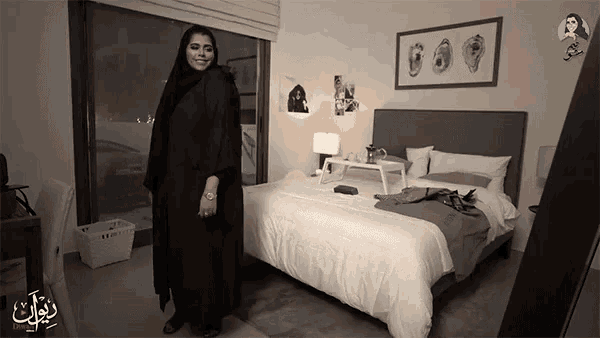 a woman in a black abaya stands in front of a bed in a bedroom