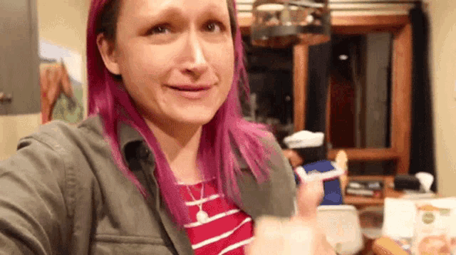 a woman with pink hair is making a funny face and giving a thumbs up sign .