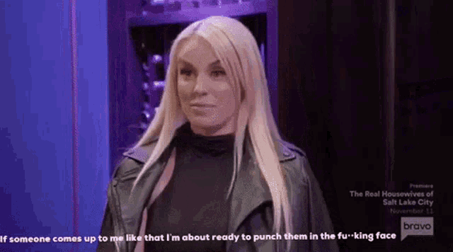 a woman in a black leather jacket is standing in front of a purple wall and talking to someone .