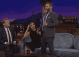 a man in a suit is dancing in front of a woman in a black dress on a couch .
