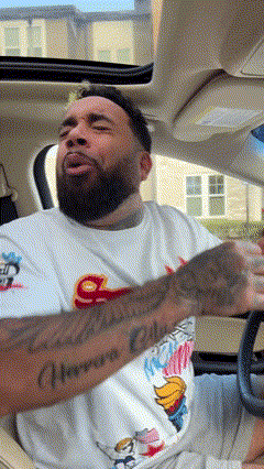 a man with a beard and tattoos is sitting in a car with his mouth open