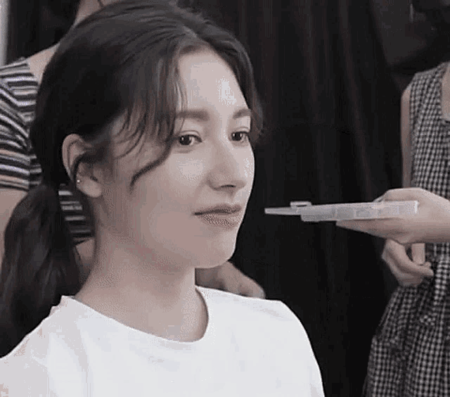 a woman is getting her hair done in a salon while another woman holds a syringe to her face .