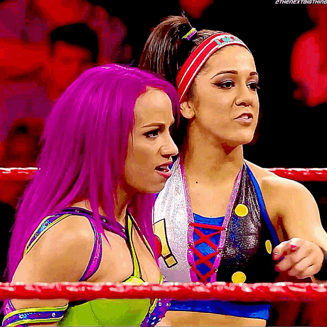 two women with purple hair are in a wrestling ring and one of them is pointing at the camera