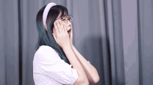 a girl with glasses and a pink headband covering her face with her hands