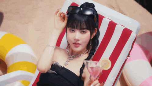 a woman is laying on a striped beach chair holding a martini glass .
