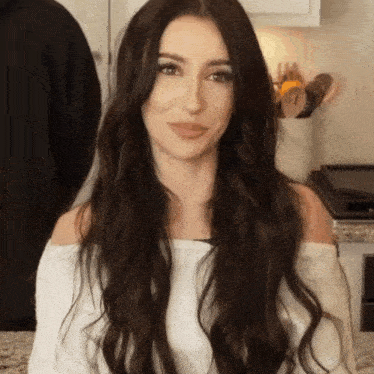 a woman with long dark hair wearing a white off the shoulder sweater