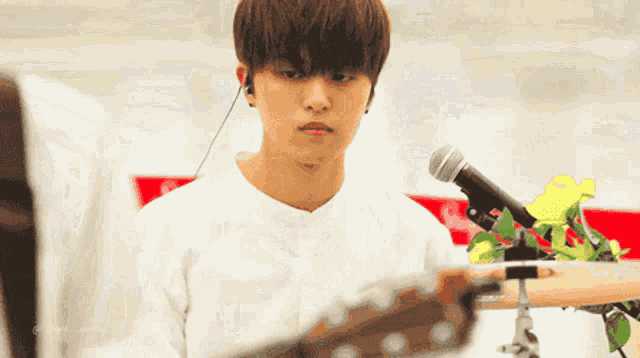a young man in a white shirt is holding a guitar in front of a microphone