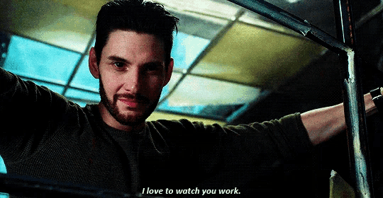 a man with a beard says " i love to watch you work " in front of a window