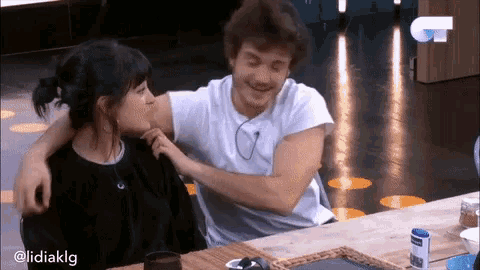 a man and a woman are sitting at a table and hugging .