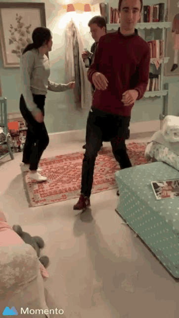 a group of people are dancing in a living room with a momento icon in the corner