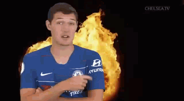 a man in a blue soccer jersey is pointing at a fire in the background .