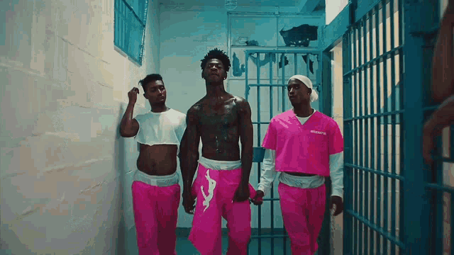 three men in pink prison uniforms walk through a hallway