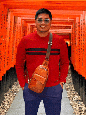 a man in a red sweater and sunglasses stands in front of a row of orange gates
