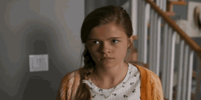 a young girl wearing a yellow cardigan and a white shirt looks at the camera