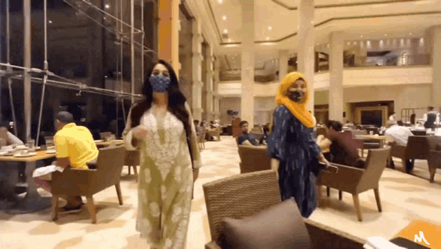 two women wearing face masks are walking through a large room