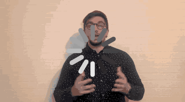 a man wearing glasses and a polka dot shirt stands in front of a white wall