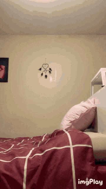 a bed with a red comforter and a pink pillow in a bedroom with a heart shaped decoration on the wall
