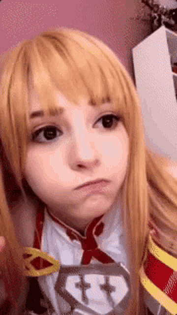 a girl with blonde hair and black eyes is wearing a cosplay costume and making a funny face .