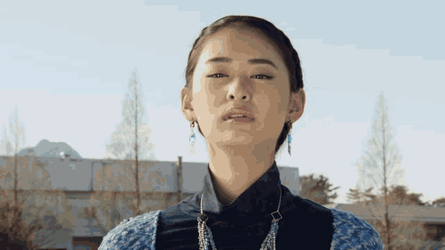a woman wearing a blue and black sweater and earrings looks at the camera