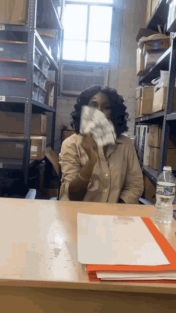 a woman is sitting at a desk with a bottle of water and a folder that says " project " on it
