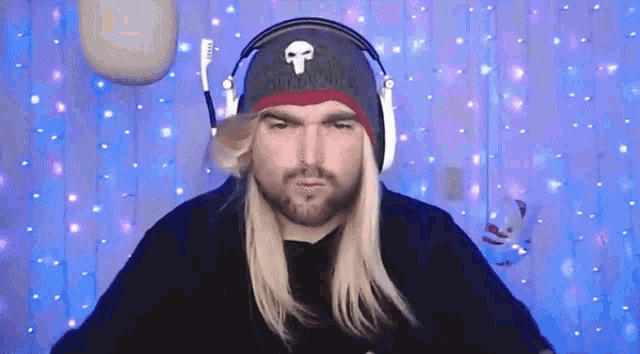 a man with long blonde hair and a beard wearing headphones and a punisher hat